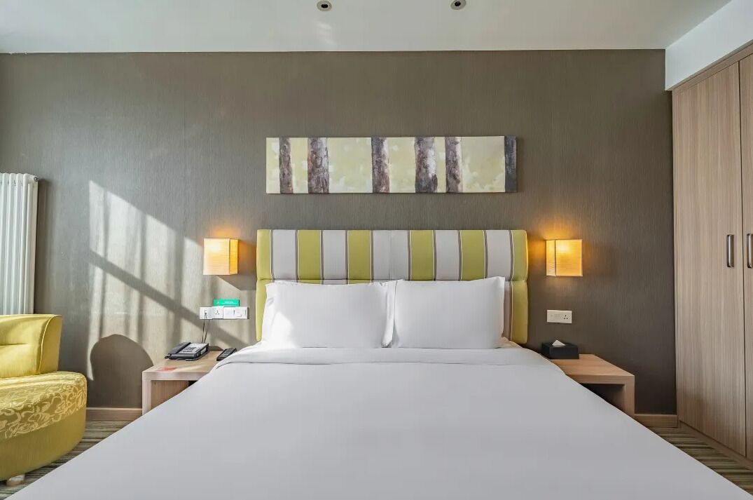 Een hotelkamer met een groot bed, twee bedlampjes, een nachtkastje, een telefoon en een stoel.