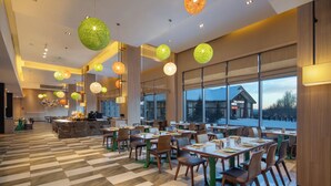 A spacious dining area with multiple tables and chairs, large windows offering a view of the outside, and hanging spherical light fixtures. - Wanda Yue Changbaishan (Baishan)