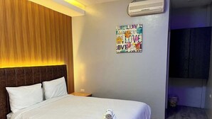 A hotel room with a bed, a nightstand, a wall-mounted air conditioner, and a decorative wall piece. - Apple Mango Resort (Silang)