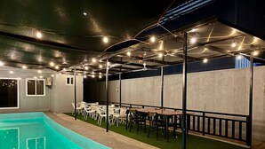 An indoor pool area with a tiled floor, surrounded by tables and chairs, and a ceiling with exposed beams and string lights. - Apple Mango Resort (Silang)