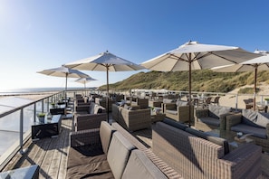 Relax in comfort with ocean views from this outdoor seating area, featuring wicker furniture and umbrellas.