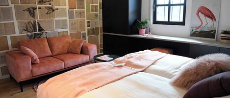 Un dormitorio ordenado con cama, sofá, una mesita y ventana con vistas.