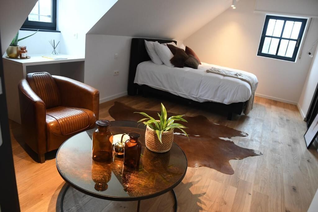 A bedroom with a bed, a leather chair, a round glass table, and a cowhide rug.