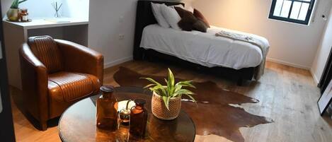 A bedroom with a bed, a leather chair, a round glass table, and a cowhide rug.