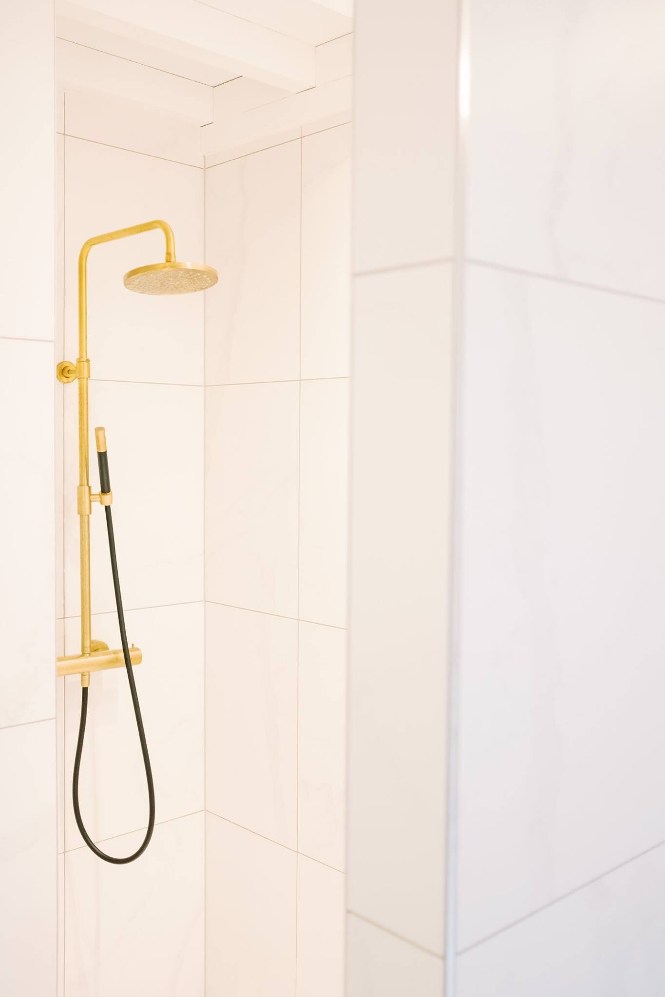 A modern shower with a gold-colored showerhead and handle, mounted on a wall with white tiles.