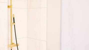A modern shower with a gold-colored showerhead and handle, mounted on a wall with white tiles.
