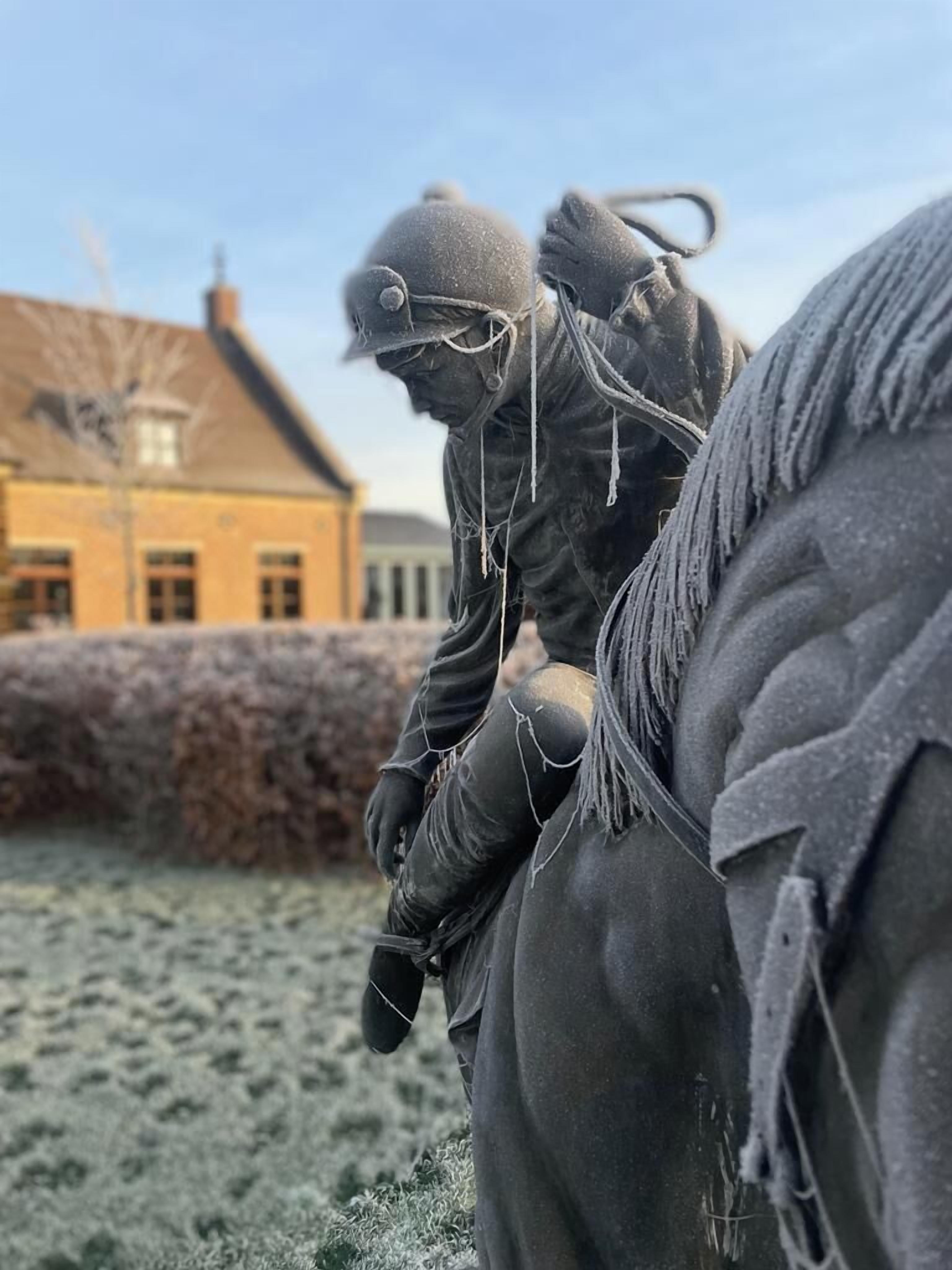 Une statue représentant une personne à cheval, avec un bâtiment en arrière-plan.