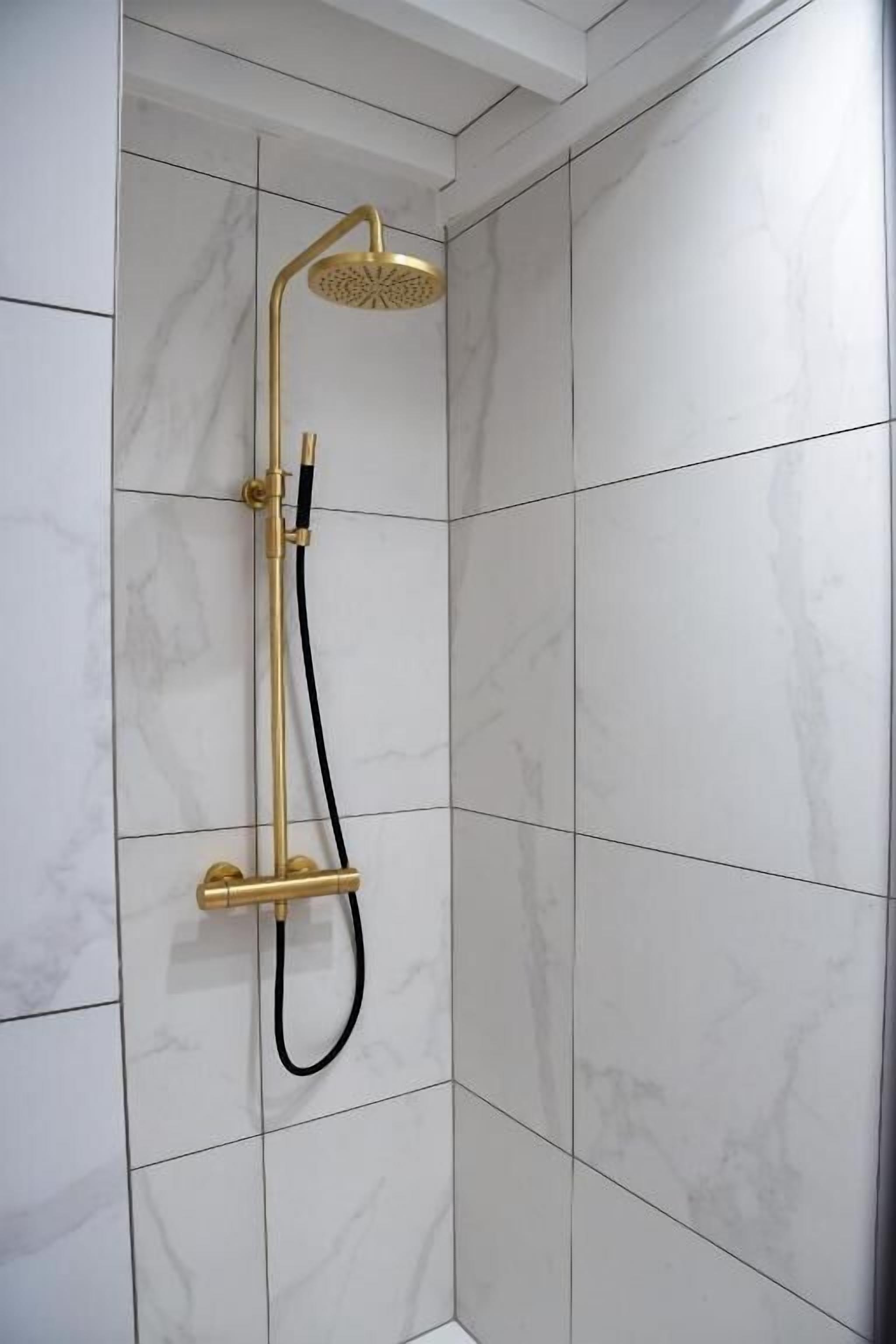 Een douche met een gouden douchekop en slang, bevestigd aan een betegelde muur.