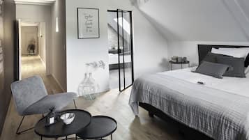 Een moderne slaapkamer met een groot bed, een grijze fauteuil, een klein tafeltje en een decoratieve vaas.
