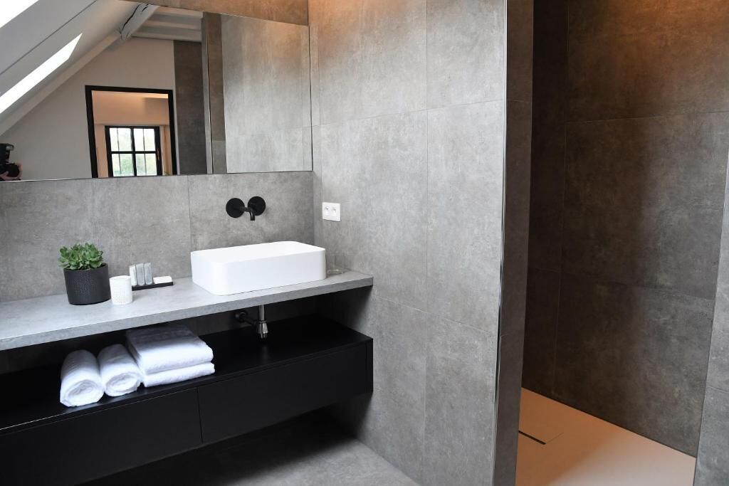 Un baño moderno con un lavamanos blanco, tocador negro y un espejo grande.