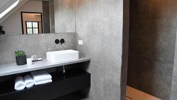 Un baño moderno con un lavamanos blanco, tocador negro y un espejo grande.