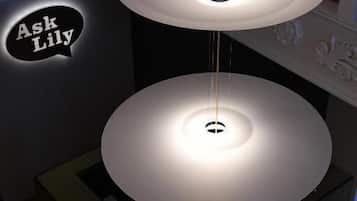 Un candelabro moderno con tres niveles, sobre un zócalo de color oscuro, en una habitación con barandilla blanca y un letrero que dice "Ask Lily".