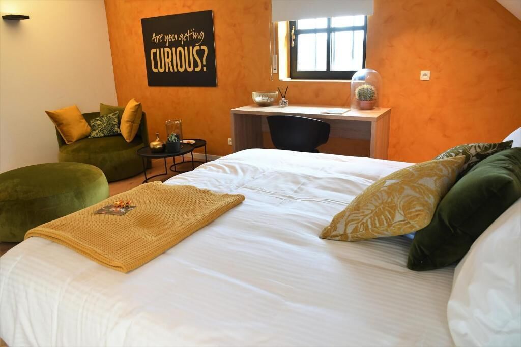 A bedroom with a bed, a desk, a chair, a green sofa, and a wall with a motivational quote.