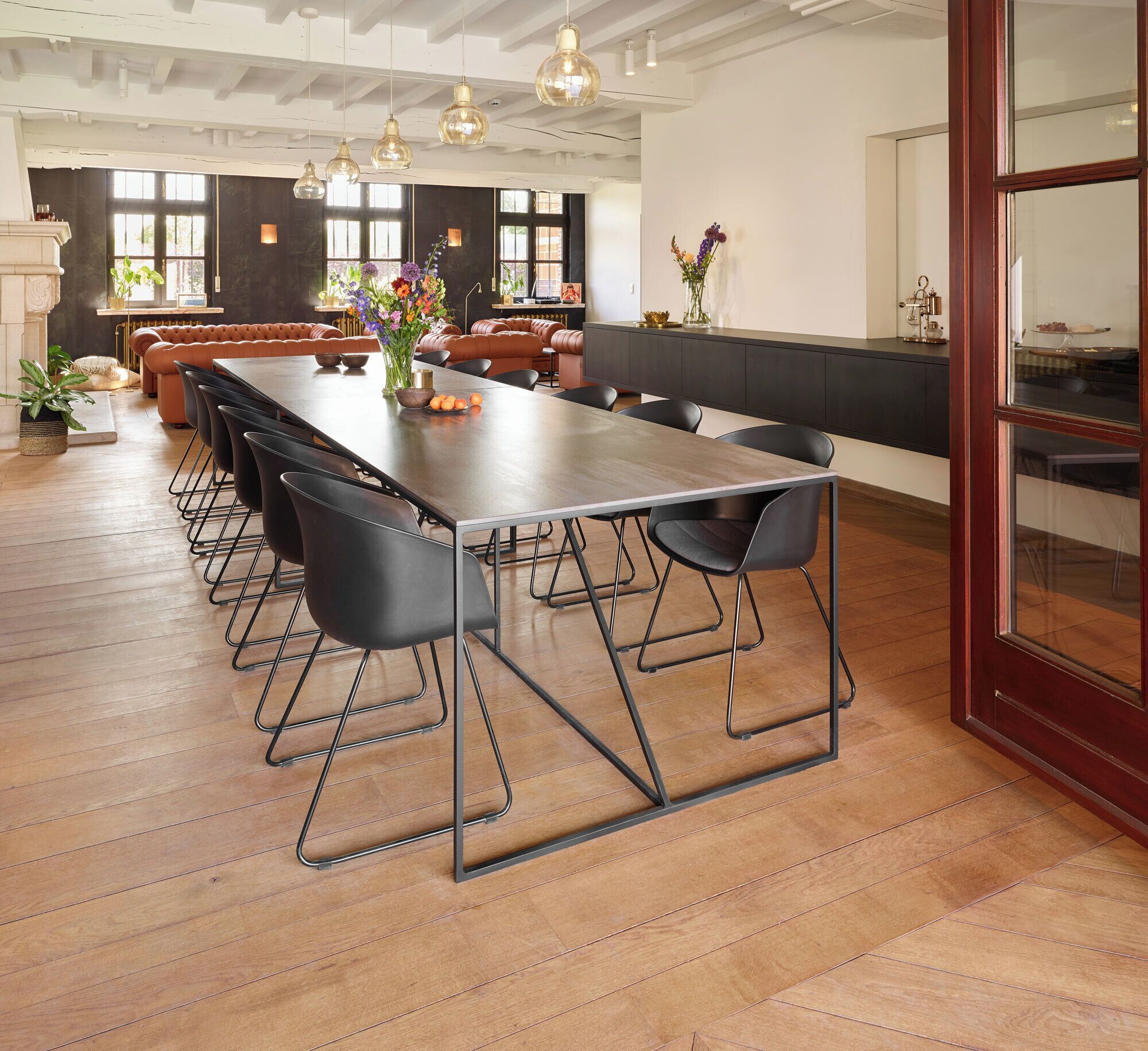 Een ruime eetruimte met een lange tafel, zwarte stoelen en hangende hanglampen.
