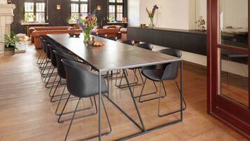 Een ruime eetruimte met een lange tafel, zwarte stoelen en hangende hanglampen.