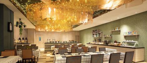 A restaurant with tables set for dining, a kitchen area, and a bar.