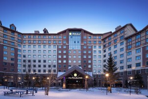 Un hotel grande con varios pisos, una entrada destacada y un área exterior cubierta de nieve con bancos.