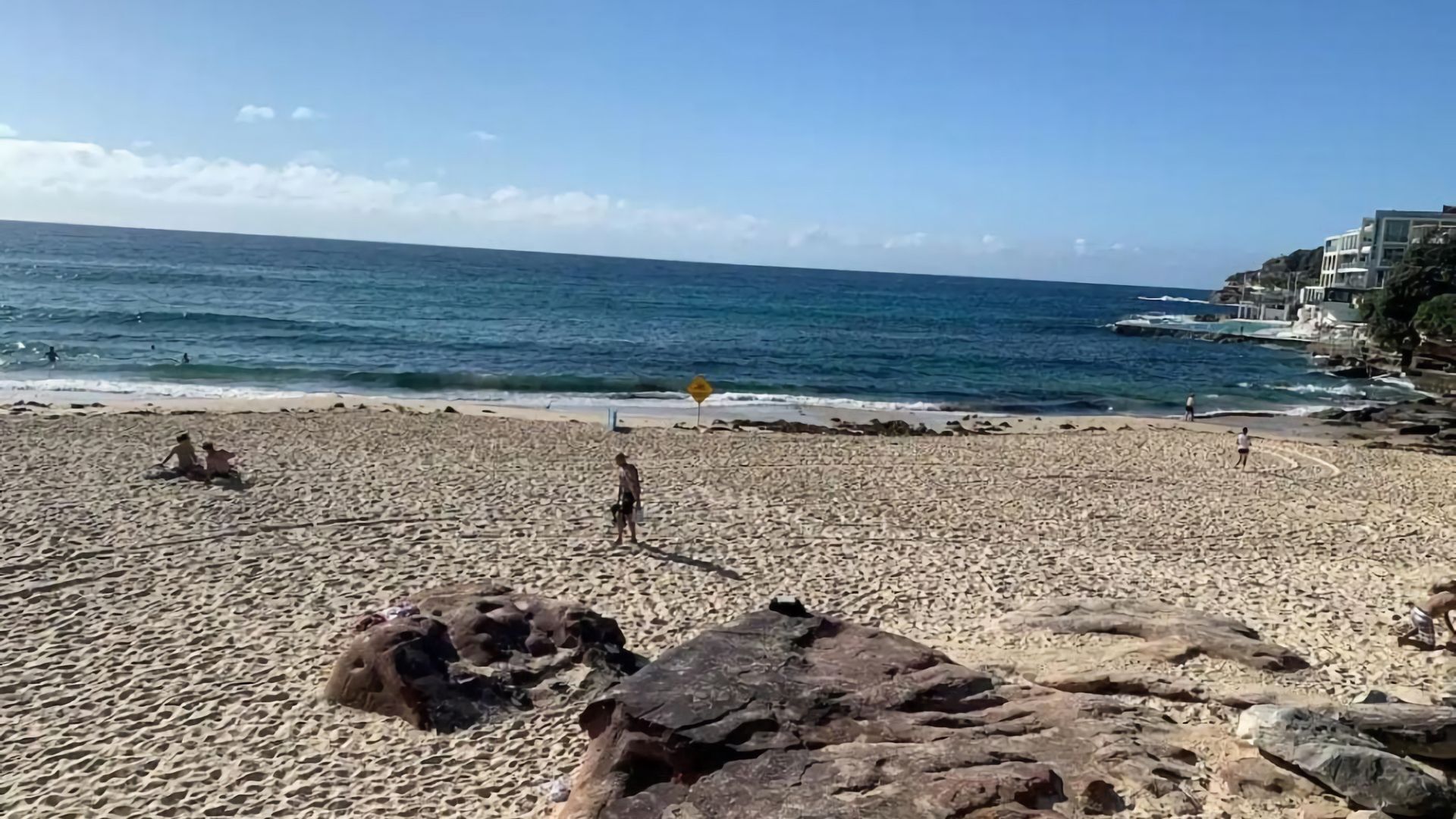 Una playa con formaciones rocosas, cielo despejado y mar tranquilo.