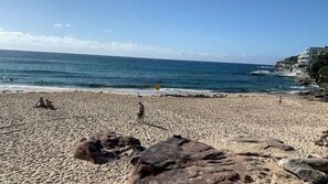 Una playa con formaciones rocosas, cielo despejado y mar tranquilo.