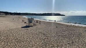 A sandy beach with a lifeguard tower, ocean waves, and a distant shoreline with buildings.