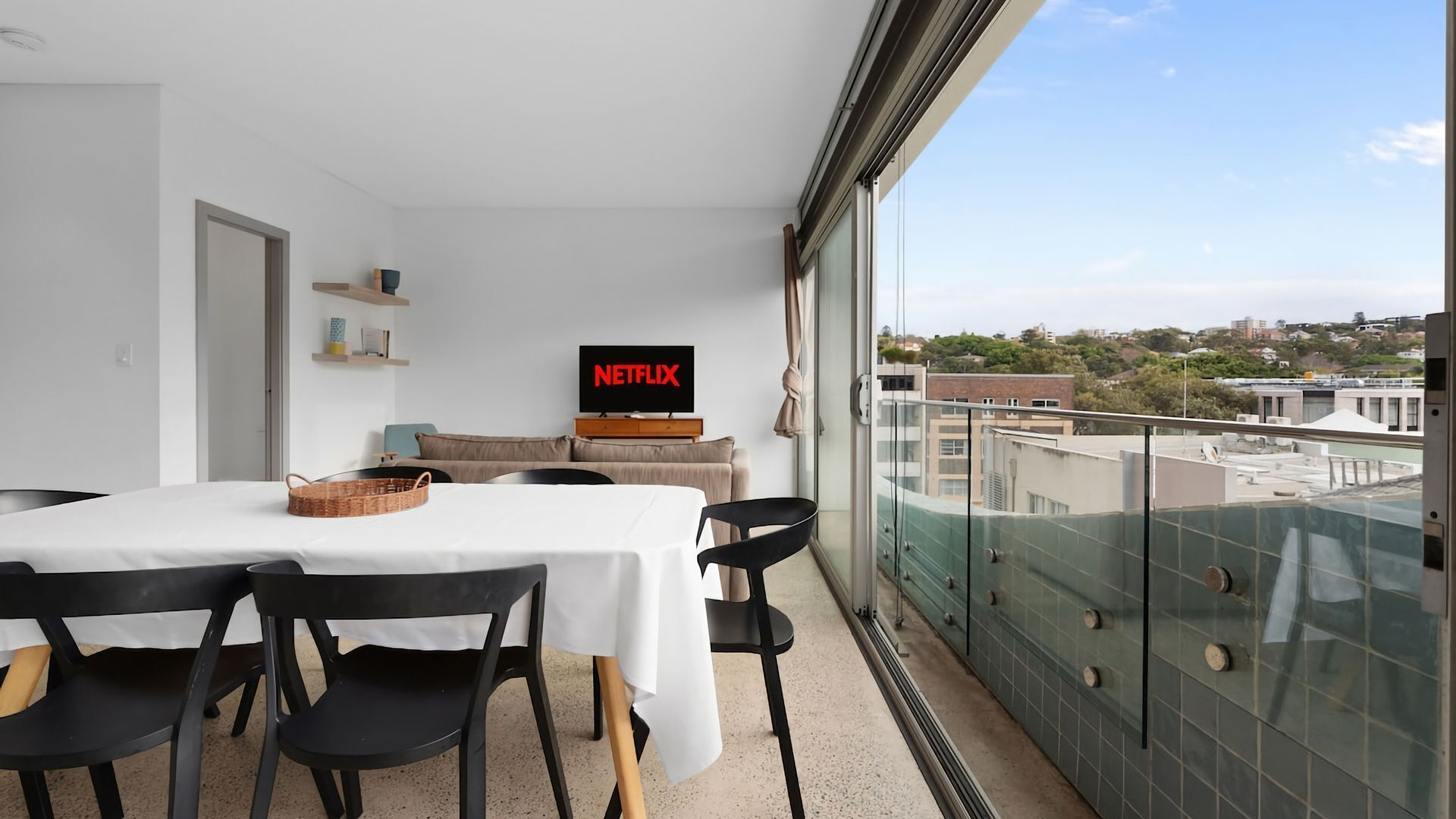 Una sala de estar moderna con comedor, televisor de pantalla plana y un balcón con vista a la ciudad.