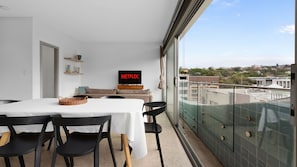 Una sala de estar moderna con comedor, televisor de pantalla plana y un balcón con vista a la ciudad.