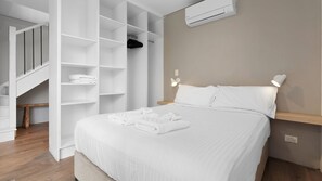 A hotel room with a bed, a built-in wardrobe, a bedside table, and a wall-mounted air conditioner.