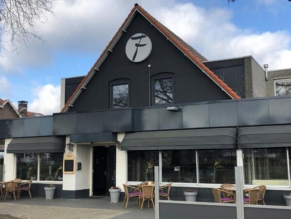 Experience the charm of this modern building, featuring a prominent clock and outdoor seating areas with wicker furniture.