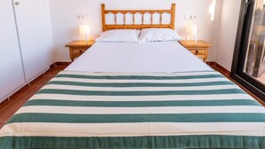 Una cama con colcha a rayas, cabecera de madera, dos mesitas de noche con lámparas y una ventana con persianas.