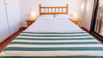 A bed with a striped bedspread, wooden headboard, two bedside tables with lamps, and a window with blinds.