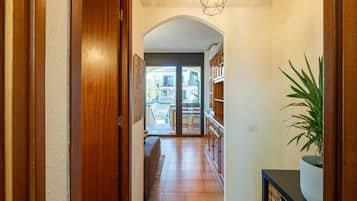 A hallway with a wooden door, a tiled floor, a geometric light fixture, and a potted plant.