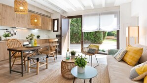 Eine moderne Küche mit Holzschränken, ein Essbereich mit Holztisch und Stühlen sowie ein gemütliches Wohnzimmer mit Sofa und Kissen.