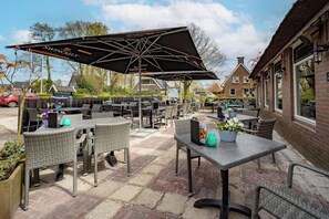 Relax under the shade of a large umbrella, surrounded by potted plants and brick paving.