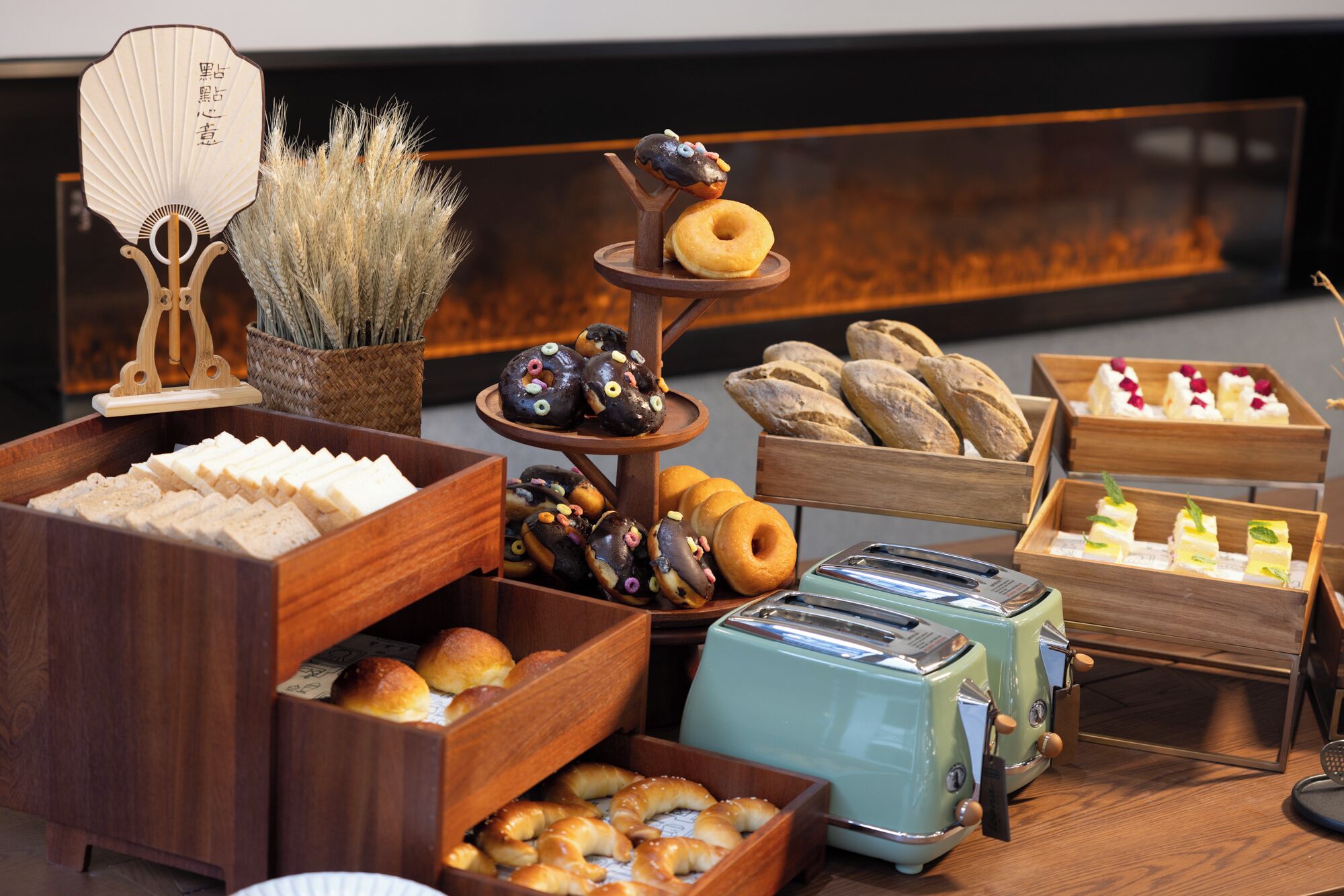 A variety of baked goods displayed on wooden stands and trays, including donuts, pastries, and bread.
