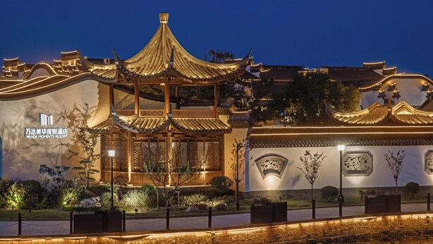 A traditional Chinese-style building with ornate architecture, a sign for Wanda Moments Resort, and a stone bridge over a reflective water surface. - Wanda Moments Xitang (Jiaxing)