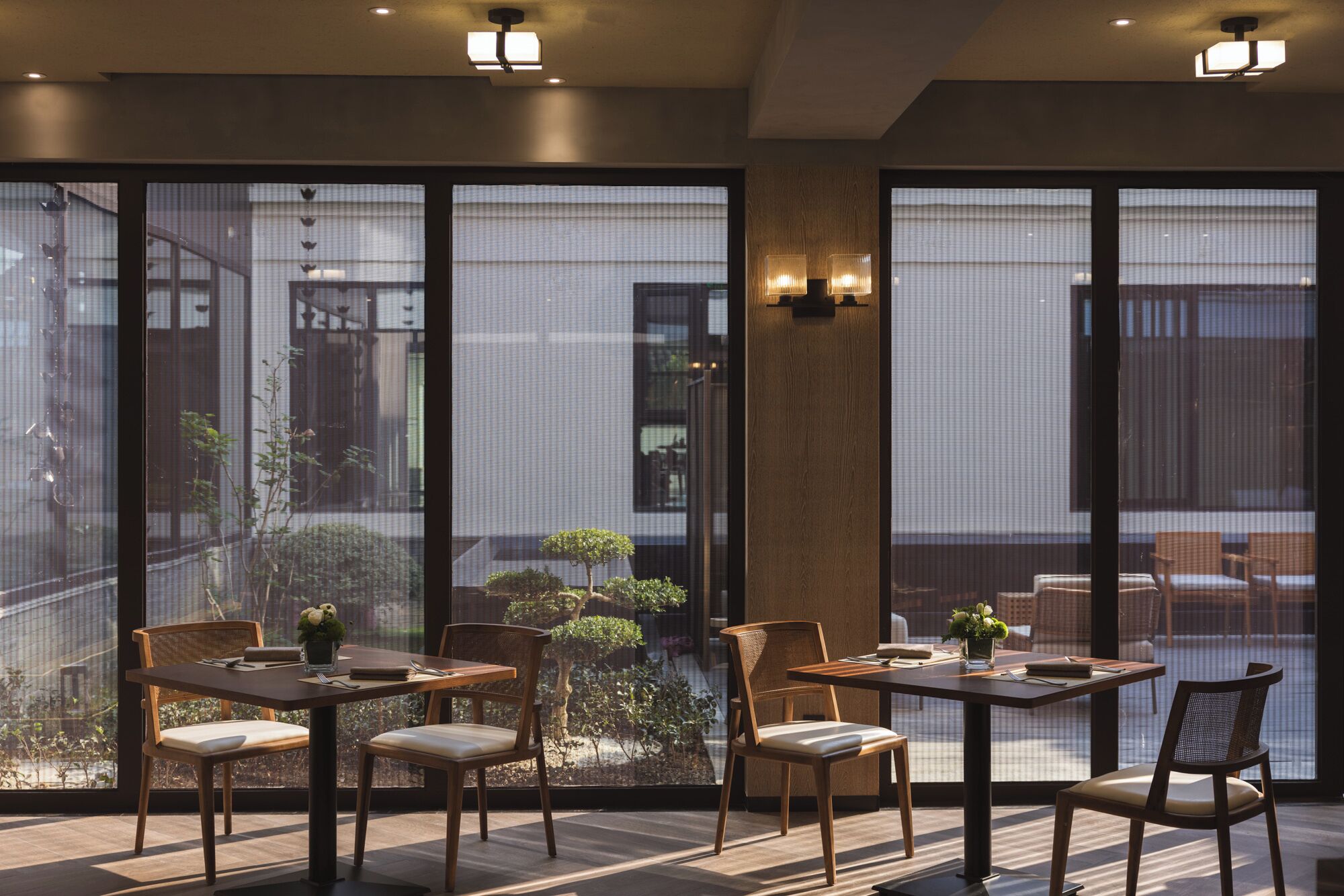 Un comedor moderno con ventanas amplias, mobiliario de madera y vistas a un jardín.