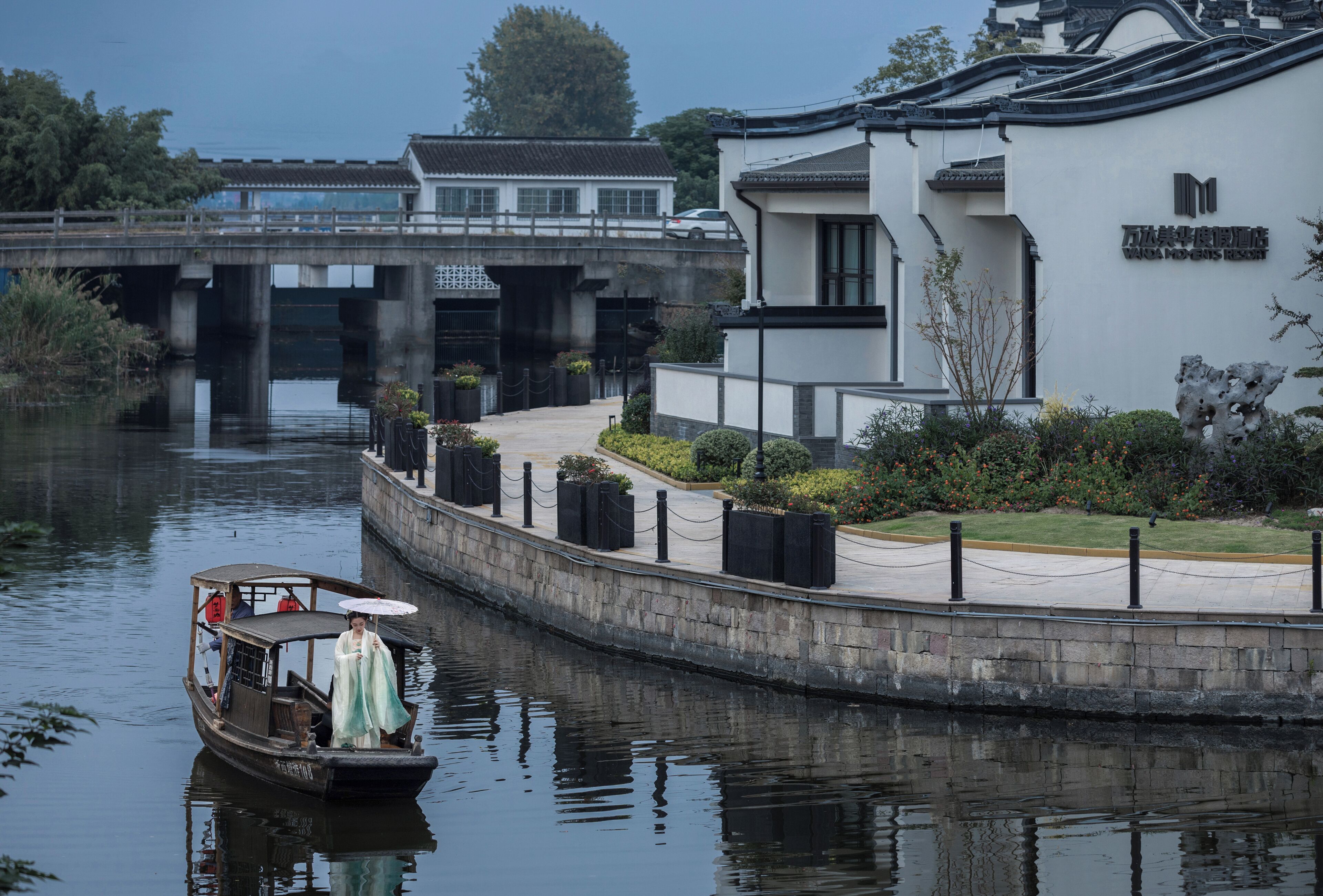 A traditional boat with passengers, a bridge, and a modern building with a sign.