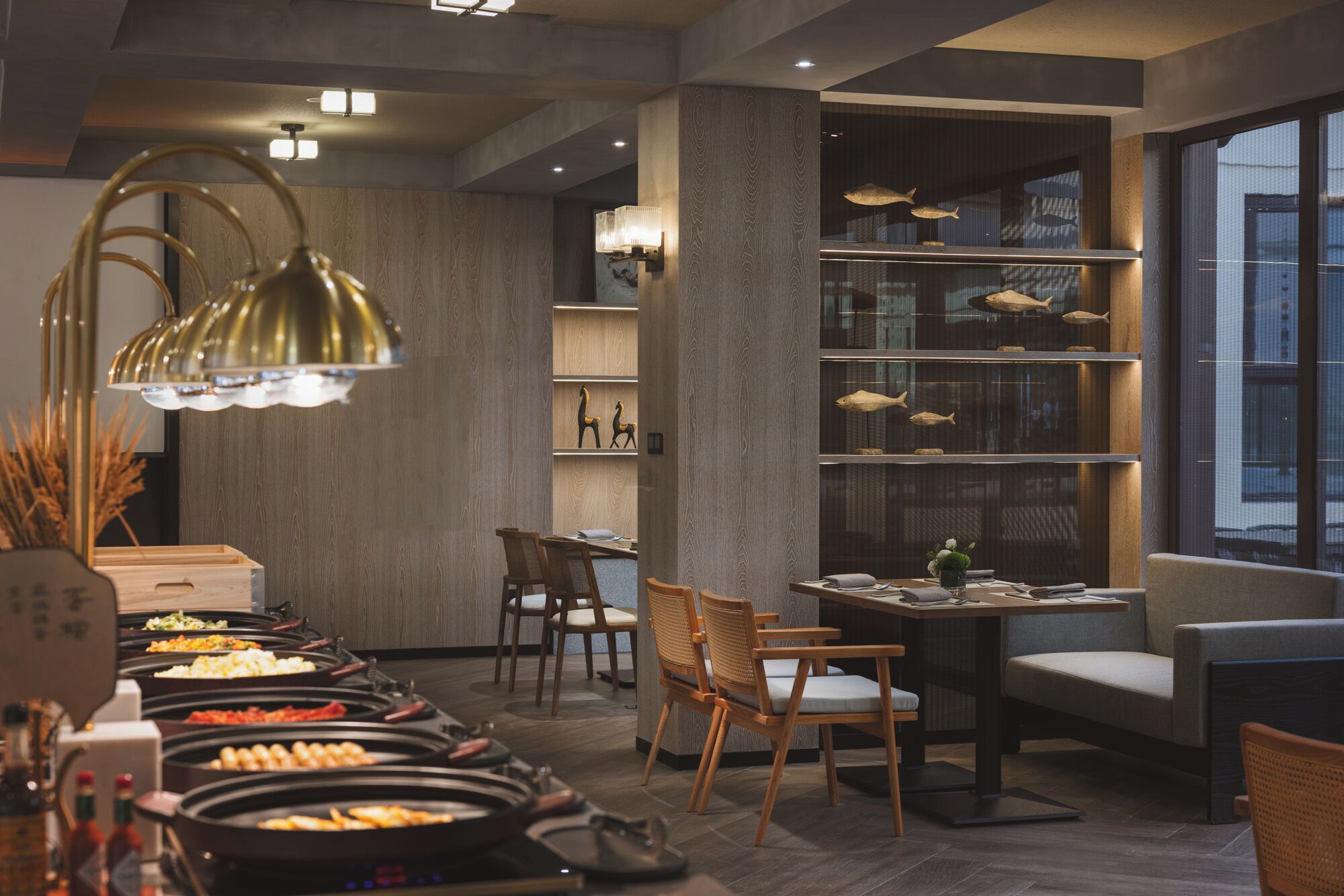 A modern restaurant with a buffet setup, wooden furniture, and a fish display on shelves.