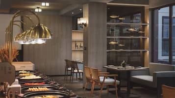 A modern restaurant with a buffet setup, wooden furniture, and a fish display on shelves.