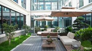 A modern outdoor patio with a wooden deck, wicker furniture, and potted plants. - Wanda Moments Xitang (Jiaxing)