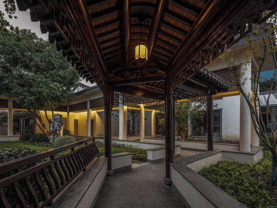 A traditional-style pavilion with a wooden roof and lanterns, surrounded by greenery and modern buildings.