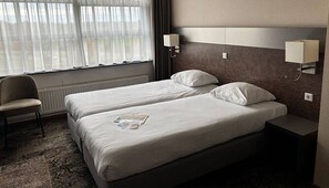 Two single beds with white linens and matching pillows, a nightstand, and a chair by the window.