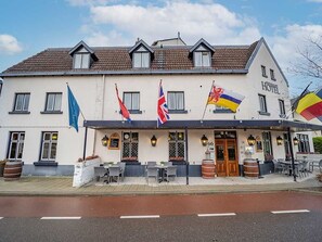 Experience the warm welcome at this traditional hotel, featuring a symmetrical facade, outdoor seating areas, and a charming entrance.