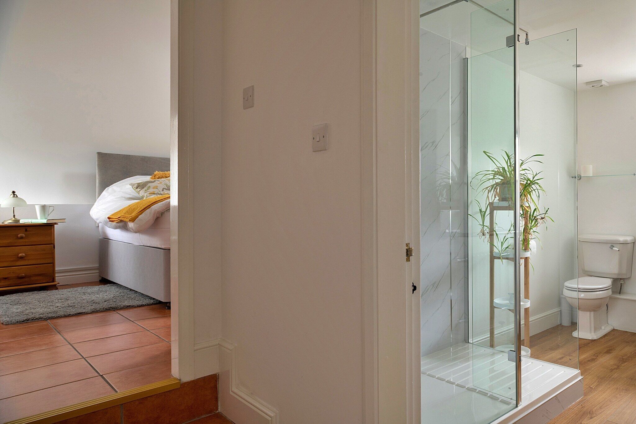 Een moderne badkamer met een douchecabine van glas, een toilet en een plant in een pot.