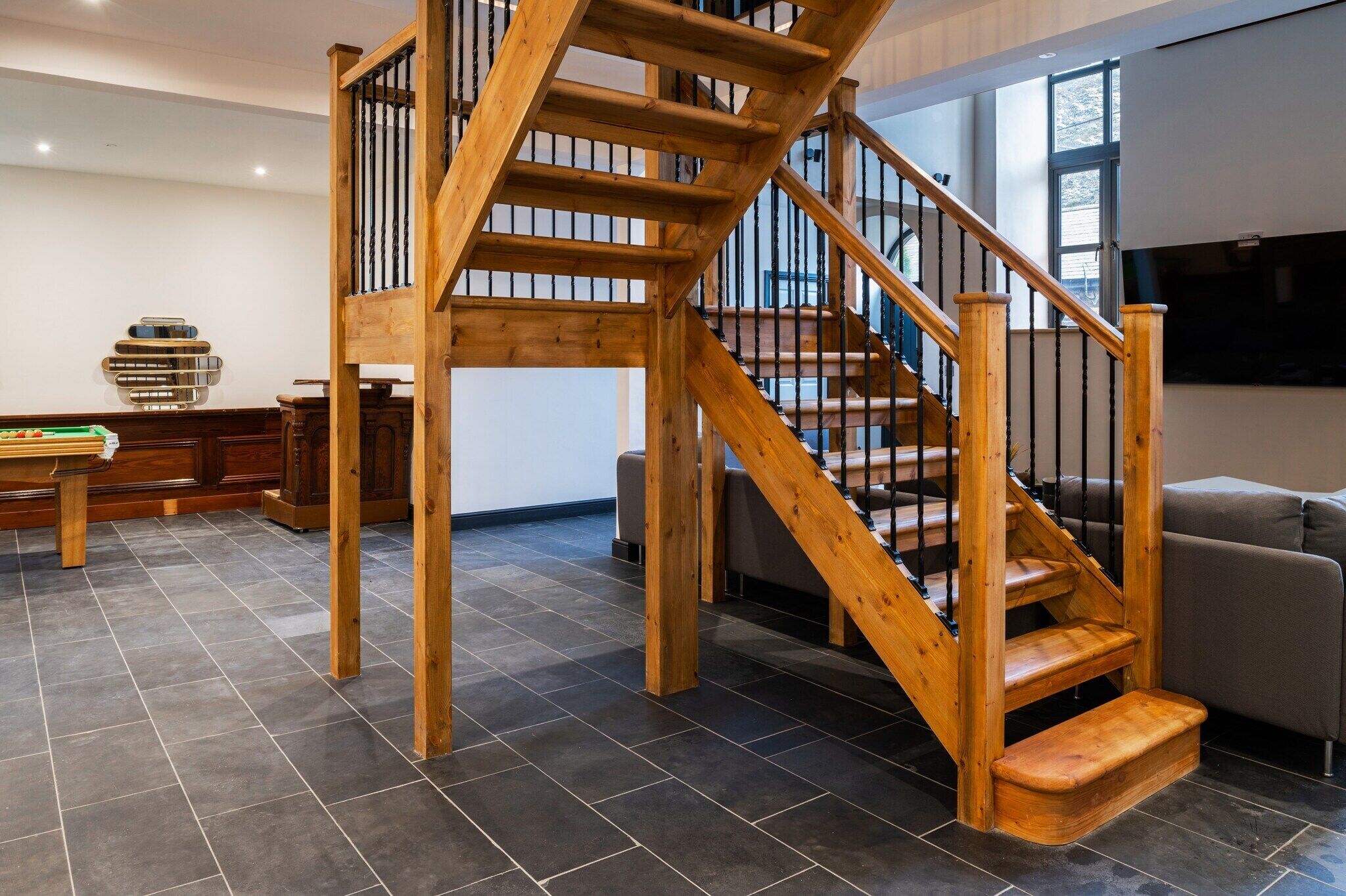 Un intérieur moderne avec un escalier en bois, un revêtement de sol en carrelage foncé et un coin salon comprenant un canapé et une table basse.