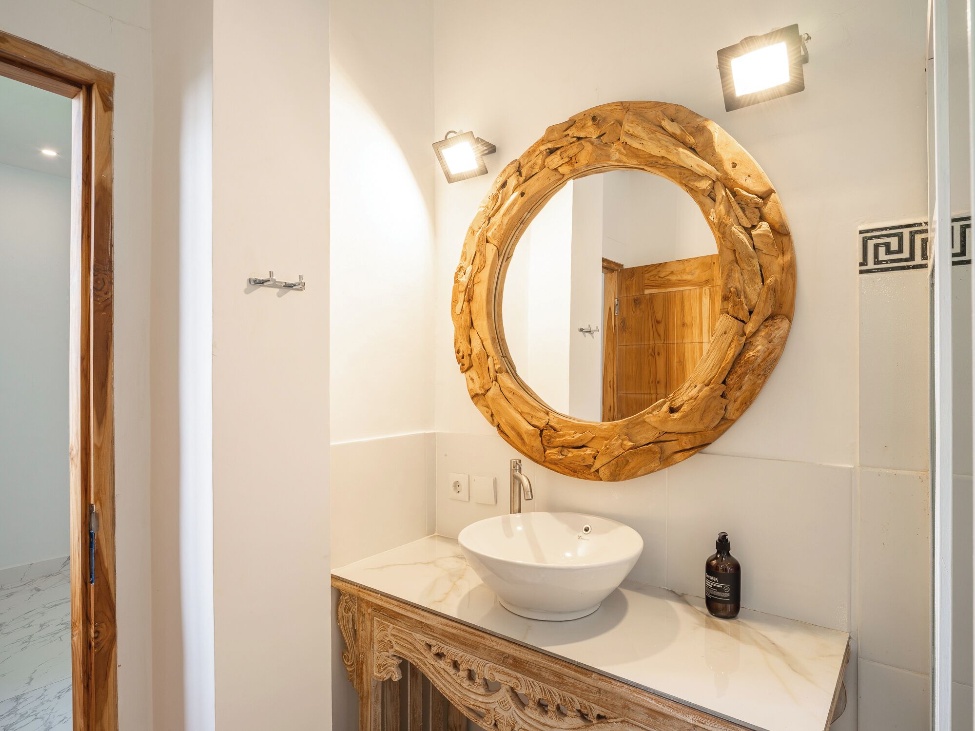 A bathroom with a wooden-framed mirror, a white sink, and a marble countertop.
