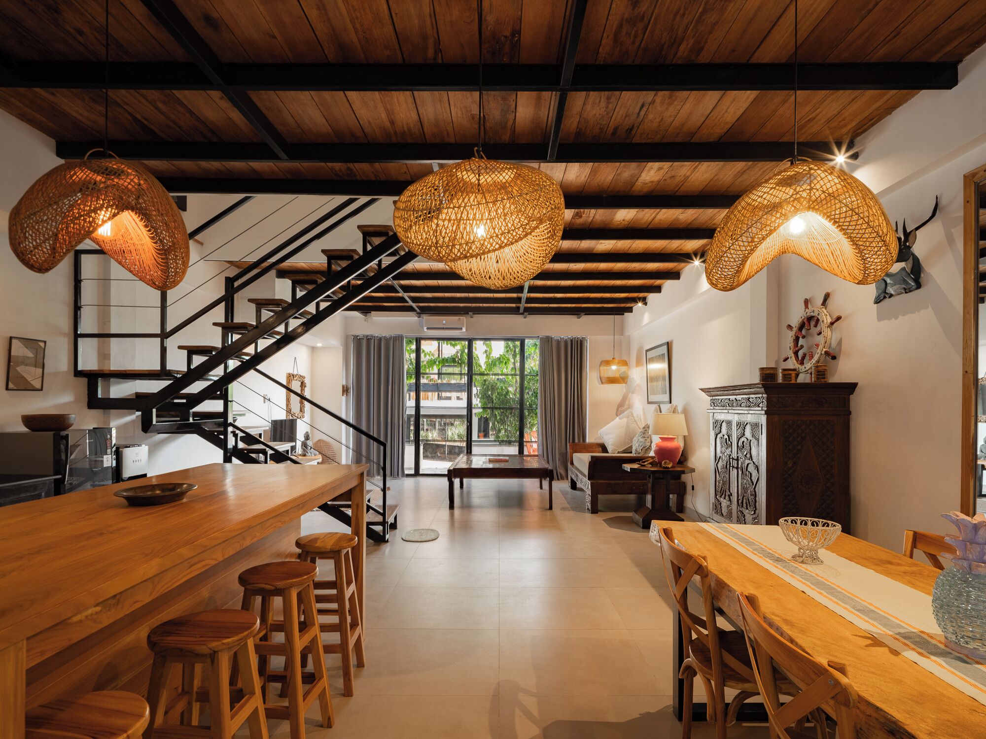 A spacious kitchen with a wooden bar and stools, a staircase, and a dining area with a table and chairs.