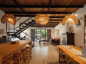 Une cuisine spacieuse avec un bar en bois et des tabourets, un escalier et un coin repas comprenant une table et des chaises.