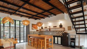 A modern kitchen with a wooden island, bar stools, pendant lights, and a stone wall.