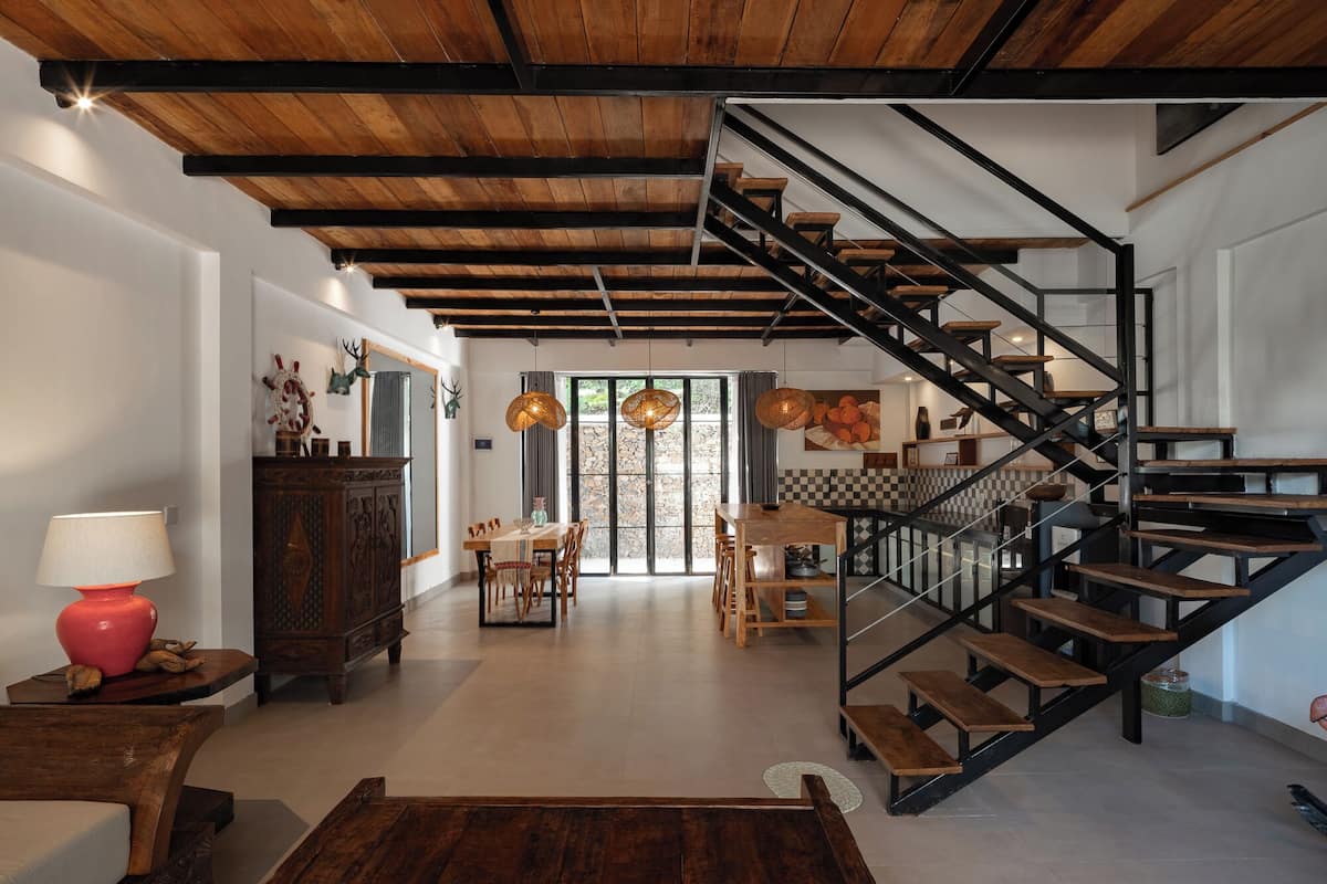 A spacious living area with a wooden staircase, a dining table, and a view of the outdoors.